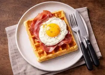 Waffle salati con uovo al tegamino e prosciutto crudo, serviti su piatto semplice per una cena veloce.