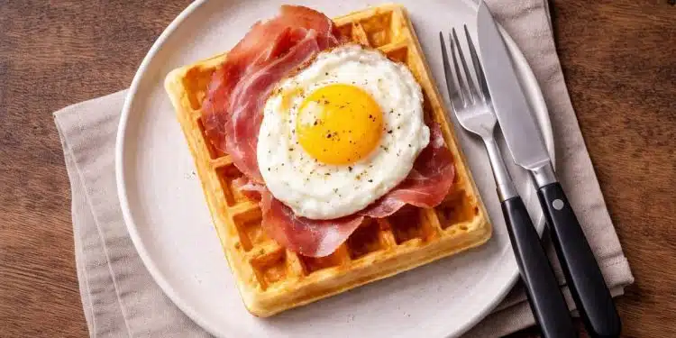 Waffle salati con uovo al tegamino e prosciutto crudo, serviti su piatto semplice per una cena veloce.