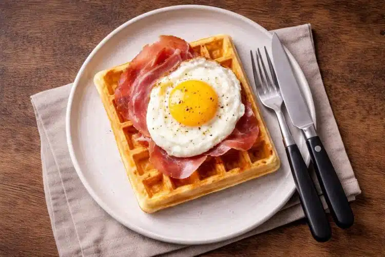 Waffle salati con uovo al tegamino e prosciutto crudo, serviti su piatto semplice per una cena veloce.